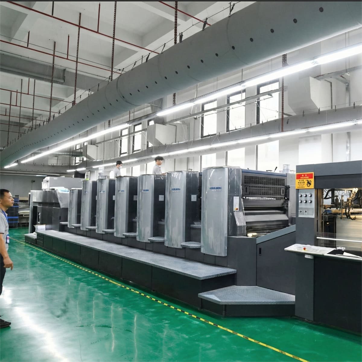 Factory workers operating printing machines at Klong Packaging's printing production facility, showcasing the production process of custom printed materials like manuals and booklets.