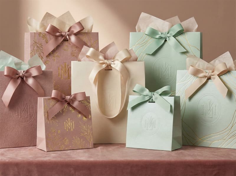 Premium gift paper bags with specialty papers, foil stamping, and ribbon handles in multiple sizes.